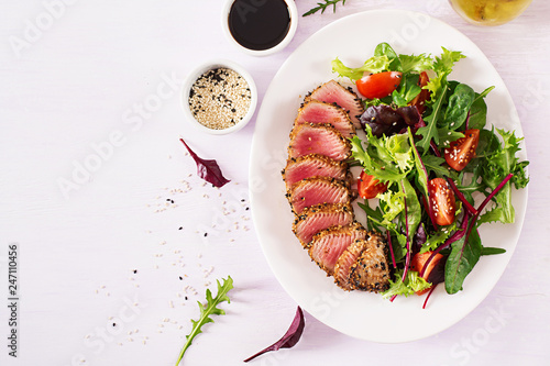 Japanese traditional salad with pieces of medium-rare grilled Ahi tuna and sesame with fresh vegetable salad on a plate. Authentic Japanese food. Top view. Copy space.