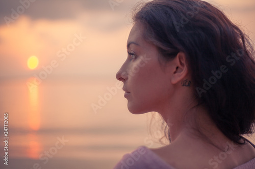 Young beautiful slim sensual woman looks at the sunset on the sea on the beach, beauty and fashion, leisure and travel concept