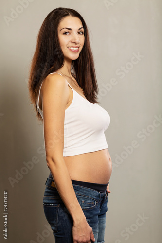 pregnancy and expectation concept - happy pregnant woman and touching her belly, gray background, portrait