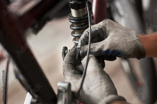 Cropped shot of male worker working in bicycle repair shop, repairing bike using special tool, wearing protective gloves