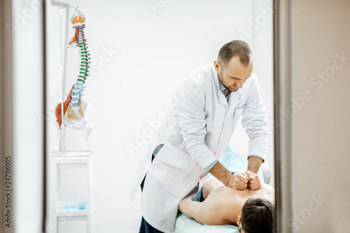 Professional senior physiotherapist doing manual treatment to a men's thoracic spine in the cabinet of rehabilitation clinic photo