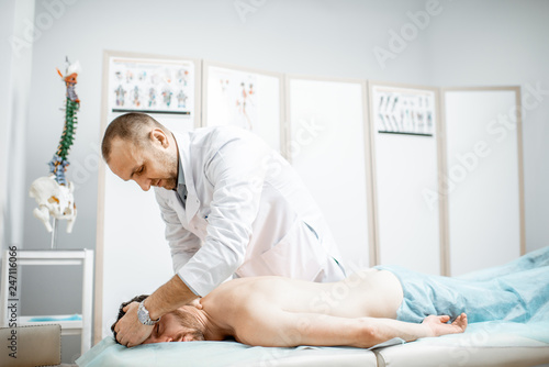 Professional senior physiotherapist doing manual treatment to a man's cervical spine in the cabinet of rehabilitation clinic