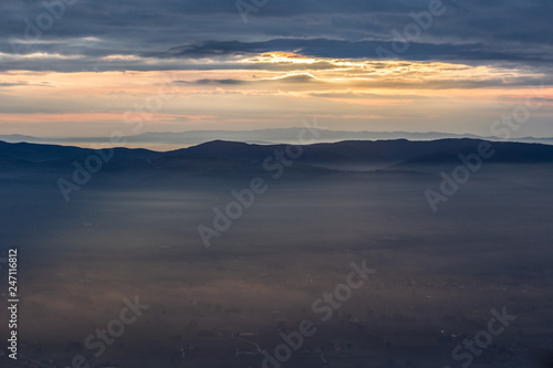 Sun rays coming down from some clouds over a valley filled by fog, illuminating part of it © Massimo