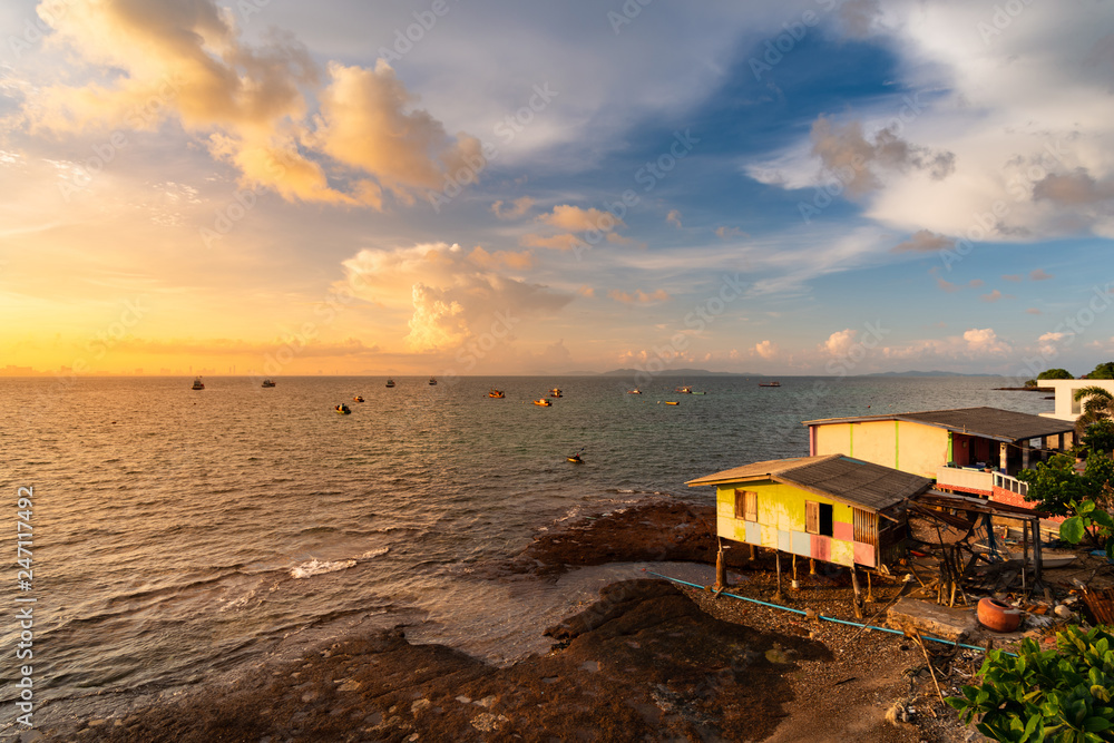 Fisherman's house is located at sea with sunrise and white clouds. Fishing boat floats in sea with sun shining. View from Koh Larn, Chon Buri THAILAND.