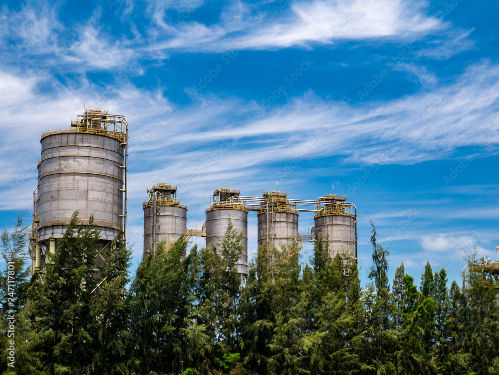 Chemical powder silos behind row of tree with blue sky.