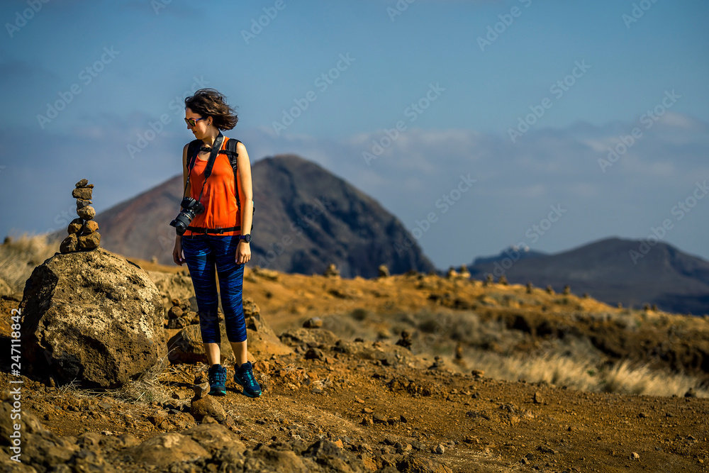 Young and attractive girl in orange shirt and blue leggings is hiking by the tourist's trail on Madeira island, Portugal. Sunny day.