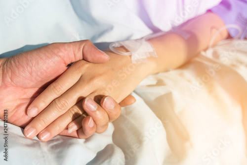 Close up. Hand of man hold hands with woman to encourage the patient saline solution in blue clothes lying on the hospital bed. Provide vascular nutrients.