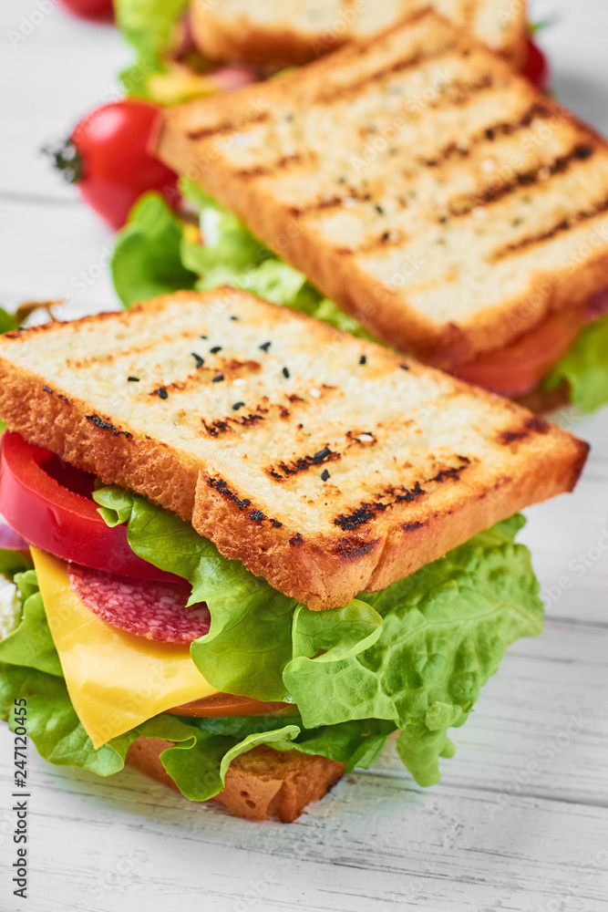 Three sandwiches with ham, lettuce and fresh vegetables on a white background Three sandwiches with ham, lettuce and fresh vegetables on a white background