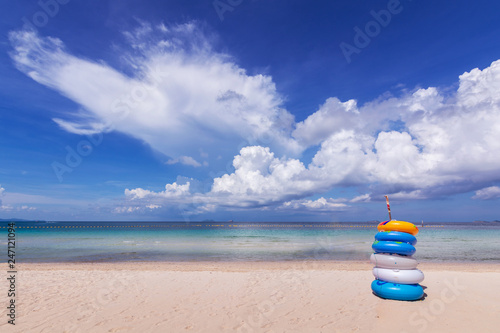 Colorful rubber ring stacked on white sand beach, blue sea and sky with white cloud.