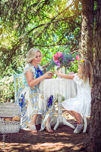 Beautiful mother and daughter have breakfast at beautiful table in summer park