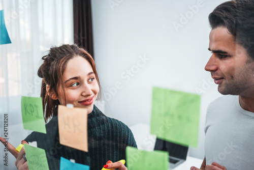 Smiling coworkers people brainsorming new business plan posted on a sticky glass note wall. Team of HR manager having meeting standing behind stiky glass wall photo