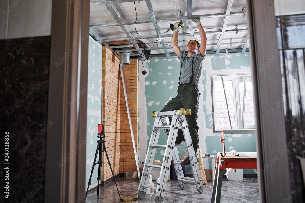 Fototapeta premium Room repair. Interior finish. young builder makes a plasterboard ceiling, standing on a stepladder