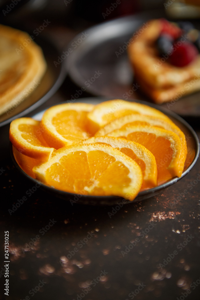 Close up on fresh orange slices placed on ceramic saucer on dark rusty table. Selective focus. Healthy breakfast ingredient.