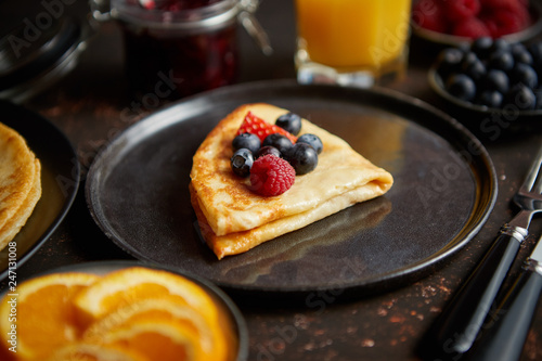 Tasety homemade pancake on black ceramic plate. Placed on dark rusty table. With fresh fruits, orange juice and marmalade. Top view, Flat lay. photo