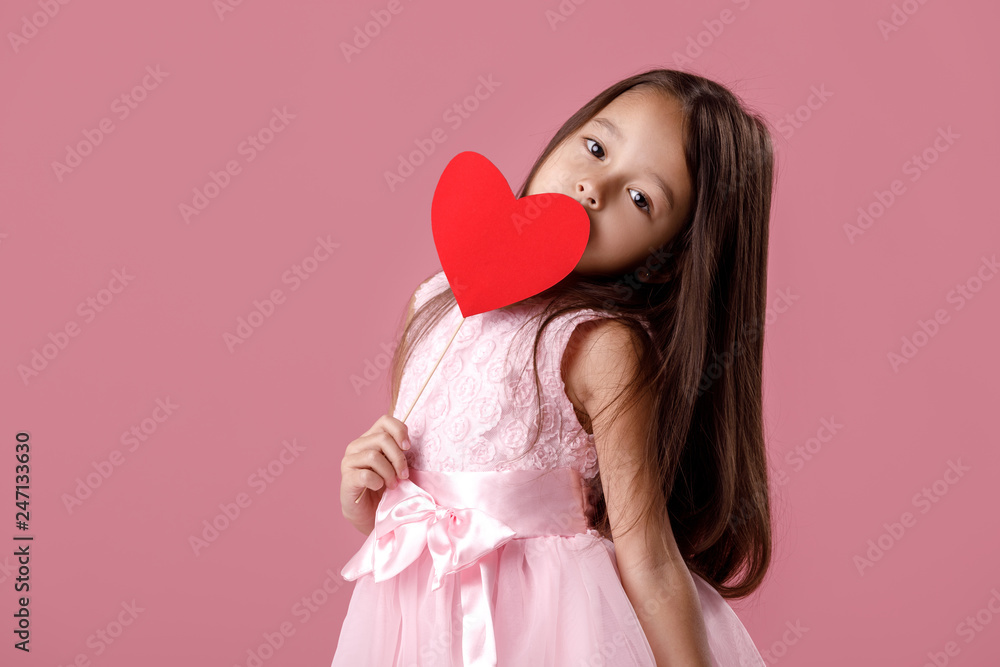 portrait of a cute little girl in a pink dress holding a paper heart on a pink background. St. Valentine's Day portrait of a cute little girl in a pink dress holding a paper heart on a pink background. St. Valentine's Day