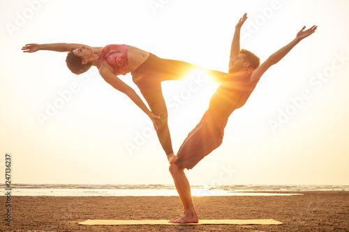 Two people practicing yoga in the sunset light on goa india beach. female and male acro yogi tantra flying copyspce photo