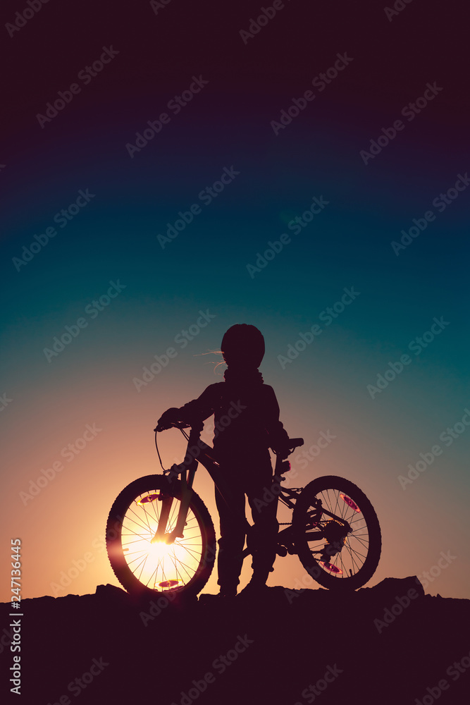 Silhouette of a little girl with a bicycle at sunset Silhouette of a little girl with a bicycle at sunset