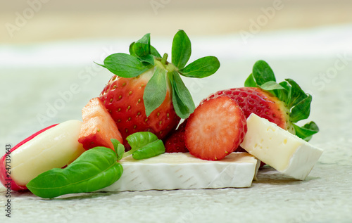 Brie cheese with strawberries and Basil close-up on a stone surface.
