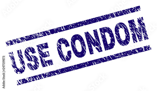 USE CONDOM seal print with scratced style. Blue vector rubber print of USE CONDOM text with dust texture. Text caption is placed between parallel lines.