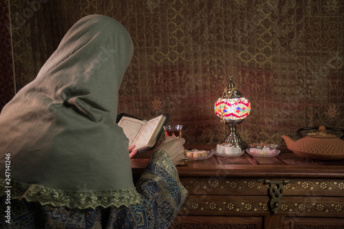 Glass of black tea in woman`s hand at Low light lounge interior with carpet. Eastern tea concept. Eastern snacks on vintage wooden surface. photo