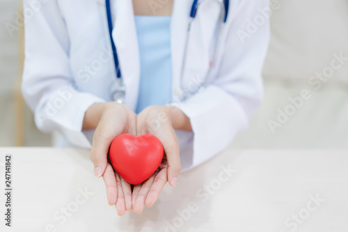 Young woman doctor holding a red heart, standing on brick wall background