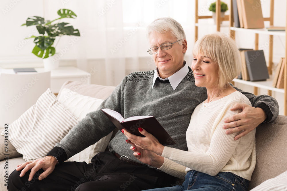 Happy old couple reading book on couch at home Happy old couple reading book on couch at home