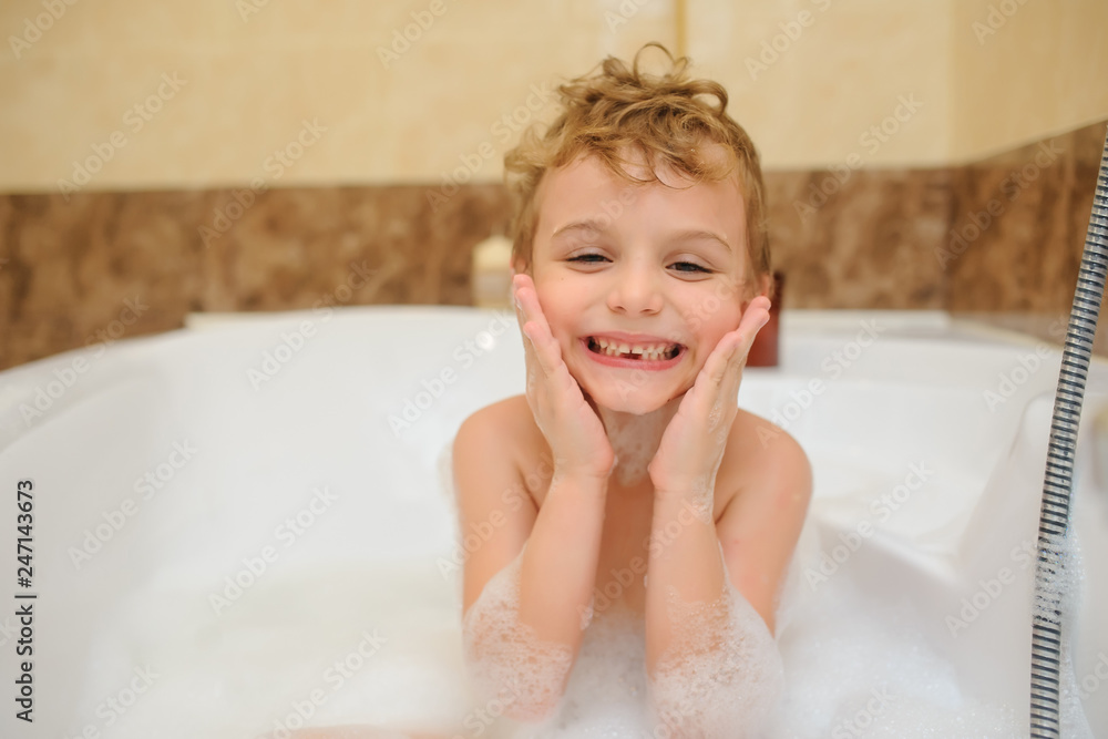 Naklejka premium Little boy washing and playing in bathtub with foam and soap bubbles