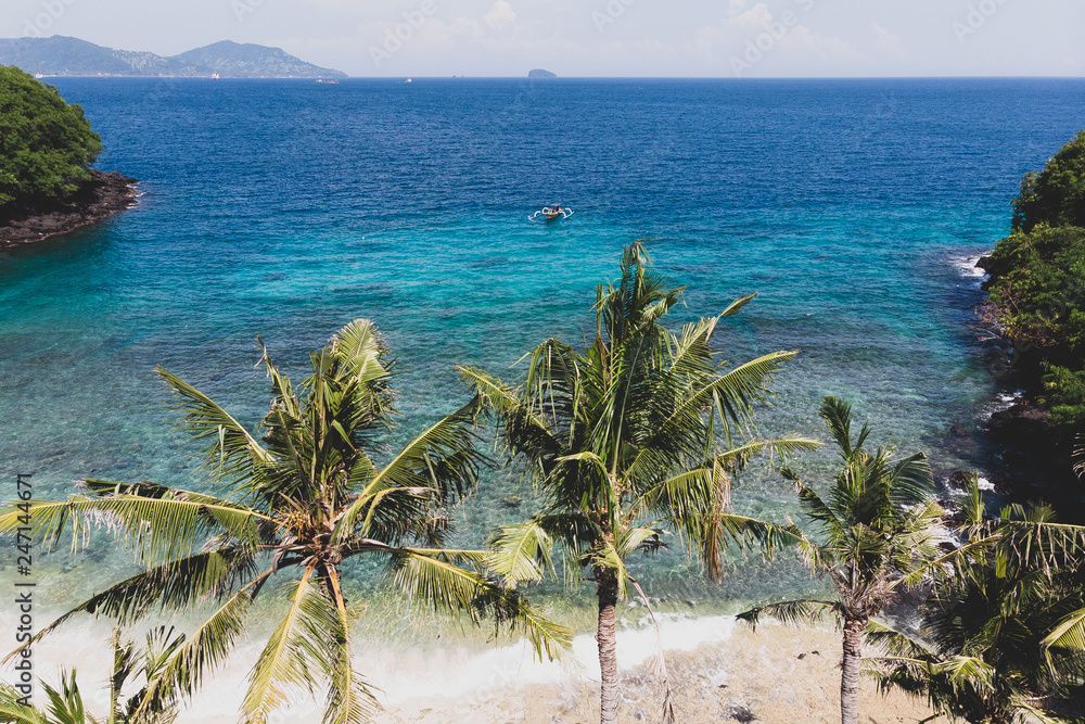 Aerial view of a tropical beach with palm trees and coastline and the boat  sways on the water of the ocean. Rainforest, blue lagoon on the island of  Bali Stock Photo