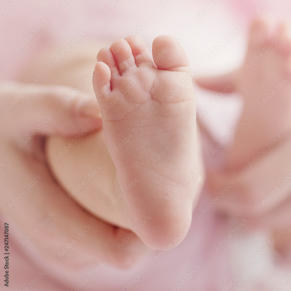 Closeup of mother hands holding cute tiny baby feet, showing baby foot.  Pink Background. Horizontal. Stock Photo