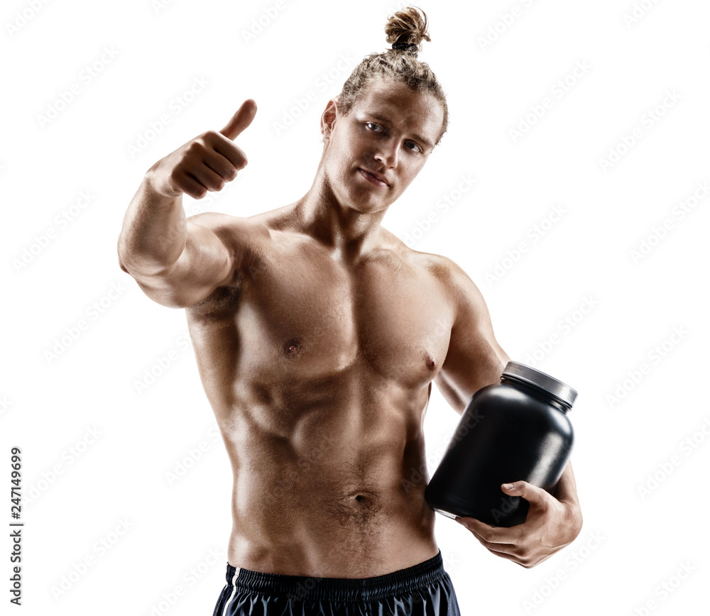 Fototapeta premium Sportsman holds big jar with sports nutrition and shows thumb up. Photo of muscular man with naked torso on white background.