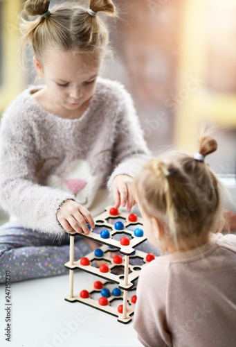 two kid girls in pink shirts with buns on their heads play educational game with small red and blue balls