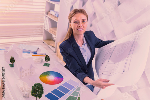 Pleasant female architect verifying blueprint at office