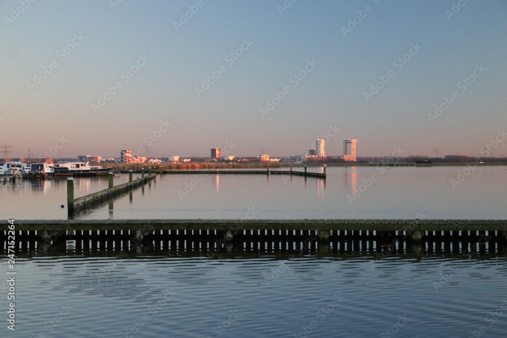 Sunset is reflecting over the water of the marina of the Rottemeren and river Rotte at Zevenhuizen with Nesselande district of Rotterdam as skyline in the Netherlands