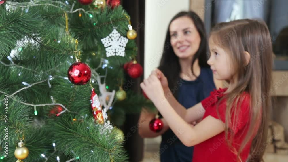 Mother and daughter decorate the Christmas tree for the new year. A woman with a child girl decorates the Christmas tree.
Mother and daughter decorate the Christmas tree for the new year. A woman with a child girl decorates the Christmas tree.