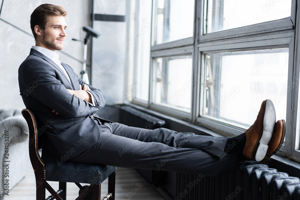 Portrait of confidence. Thoughtful young man in full suit looking away while sitting on the stool. Portrait of confidence. Thoughtful young man in full suit looking away while sitting on the stool.