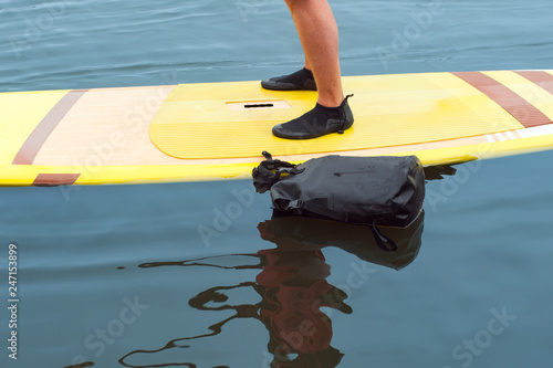 Male legs on floated paddleboard and waterproof bag with stuff