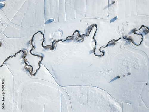 Aerial view of meandering river on snow covered ground. White fields with curved brook flowing through © Mario