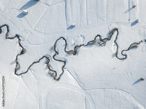 Aerial view of meandering river on snow covered ground. White fields with curved brook flowing through