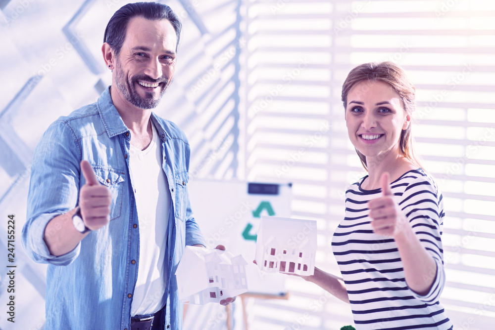 Fototapeta premium Two people smiling and putting thumbs up while standing with little houses