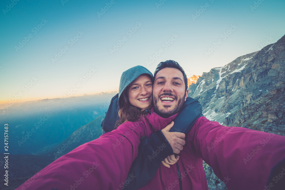 Couple of hikers taking selfie from top of the mountain with peaks and valley view on the background after long trekking Couple of hikers taking selfie from top of the mountain with peaks and valley view on the background after long trekking