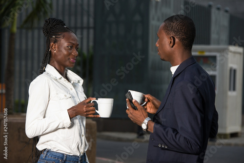 Two coworkers drinking coffee near the office building outside i