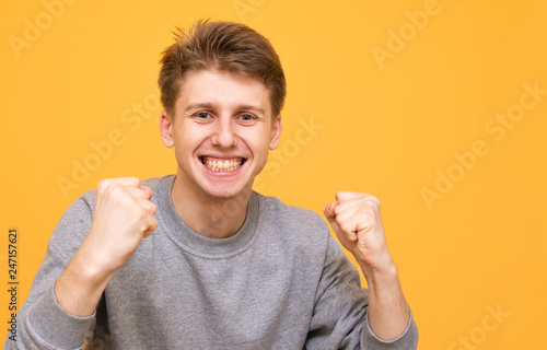 Close-up portrait of an excited guy who rejoices in winning a yellow background. Teenager rejoices with his hands raised and looks into the camera, isolated on a yellow background. Copyspace