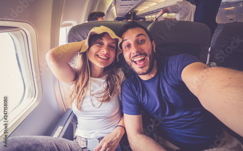 Young handsome couple taking a selfie on the airplane during flight around the world. They are a man and a woman, smiling and looking at camera. Travel, happiness and lifestyle concepts.