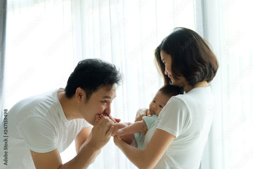 Fun and play together. Asian family, father and mother are playing with their newborn baby. Mom holding baby body while dad holding the legs and kissing the feet. They all are smiling with happiness. Fun and play together. Asian family, father and mother are playing with their newborn baby. Mom holding baby body while dad holding the legs and kissing the feet. They all are smiling with happiness.