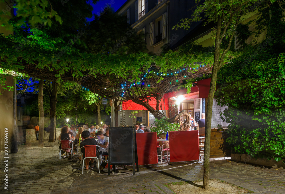 Fototapeta premium Typical night view of cozy street with tables of cafe and easels of street painters in quarter Montmartre in Paris, France