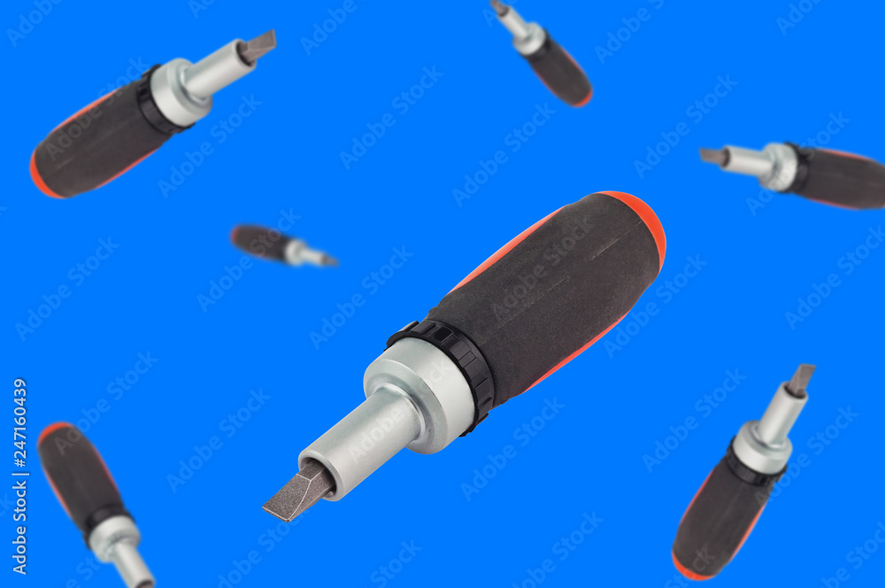 Lot of falling ratchet screwdriver with orange and black plastic with rubber handle and bit on blue background Lot of falling ratchet screwdriver with orange and black plastic with rubber handle and bit on blue background