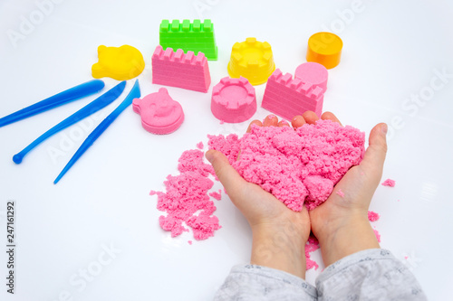 Hands of a kid playing with pink magic sand.