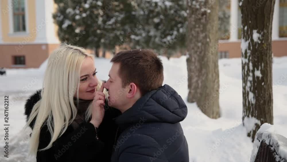 Beautiful young couple sitting on a bench cuddle talking and smiling in a city winter park. Beautiful young couple sitting on a bench cuddle talking and smiling in a city winter park.