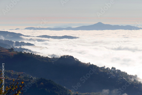 A white mist has covered Rhodope mountain in Bulgaria. Sea of thick fog. Only the high parts of the mountain can be seen. Village on the hill.