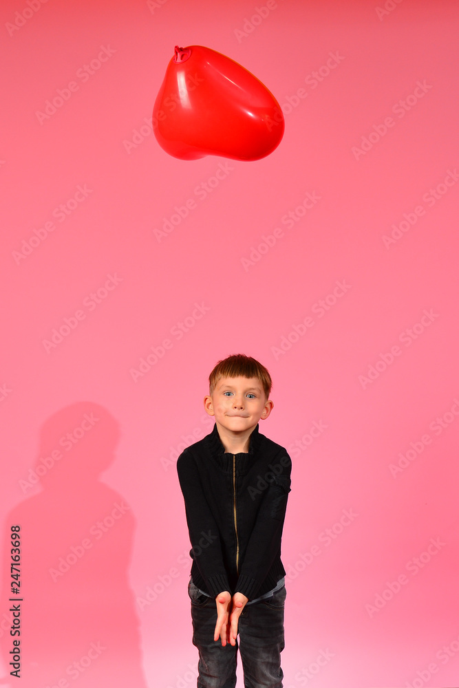 A boy throws and catches a heart-shaped balloon on a pink background in the studio. A boy throws and catches a heart-shaped balloon on a pink background in the studio.